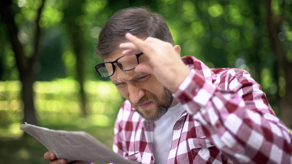 אדם מרכיב משקפיים מרחיק דף מעיניו בניסיון לקרוא